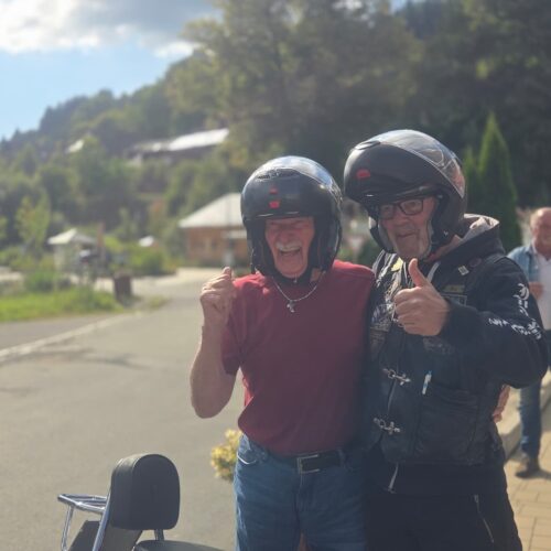 Zwei ältere Männer mit Helmen lächeln und zeigen Daumen nach oben im Sonnenschein