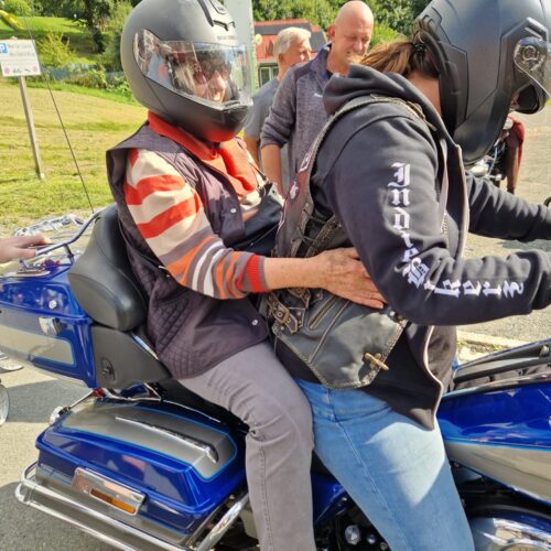 Zwei Personen mit Helmen sitzen auf einem blauen Motorrad in entspannter Stimmung