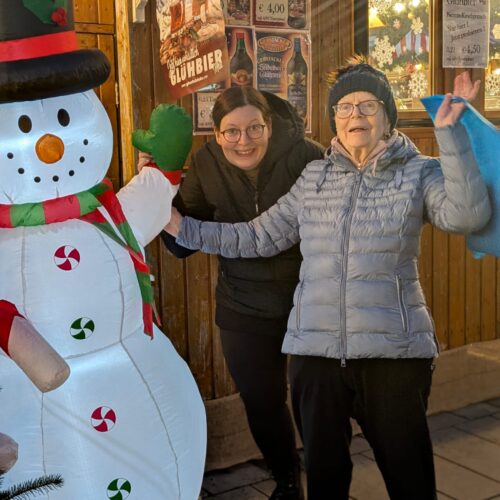 Zwei Frauen lachen fröhlich neben einem leuchtenden Schneemann mit Zylinder und Schals