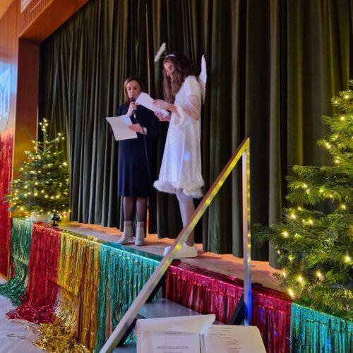 Zwei Frauen stehen auf einer bunt geschmückten Bühne und halten Texte in der Hand