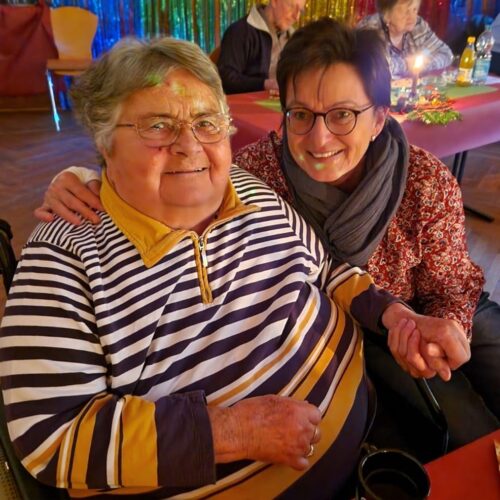 Zwei ältere Frauen lächeln herzlich bei einer festlichen Tischrunde mit bunten Dekorationen