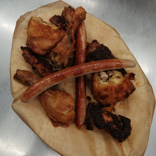 Auf braunem Papier liegen verschiedene Fleischstücke und zwei gebratene Würste