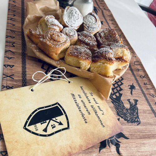 Frisch gebackene Zimtschnecken mit Puderzucker auf braunem Papier und bestickter Tischdecke