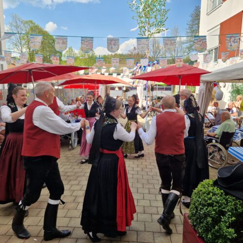 Eine Gruppe Menschen in traditioneller Tracht tanzt fröhlich im Sonnenschein auf einem Fest