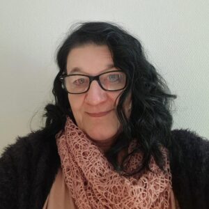 Eine Frau mit langen schwarzen Haaren und Brille lächelt freundlich vor hellem Hintergrund