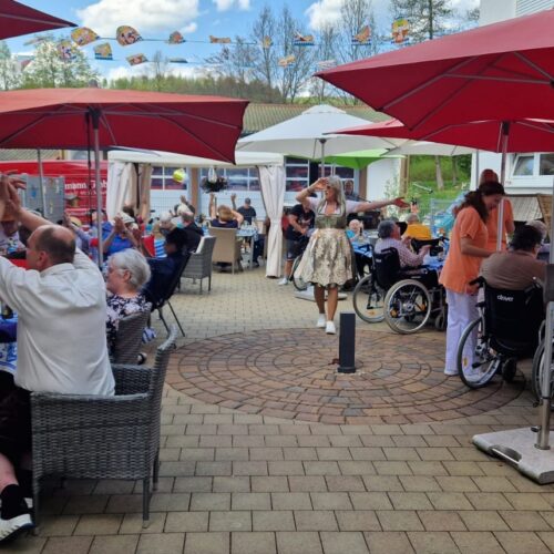 Mehrere ältere Menschen sitzen an blauweiß gedeckten Tischen im Freien und genießen das sonnige Wetter