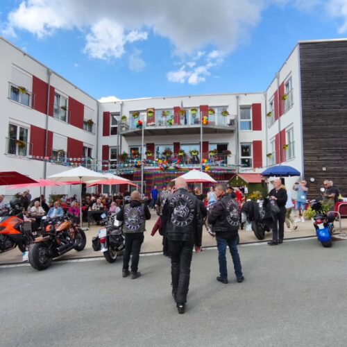 Mehrere Motorradfahrer mit schwarzen Westen gehen auf ein bunt geschmücktes Gebäude zu