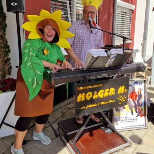 Eine fröhliche Frau im Sonnenblumenkostüm und ein lächelnder Mann spielen Keyboard