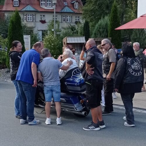 Mehrere Personen in lässiger Kleidung schauen freundlich auf ein blaues Motorrad